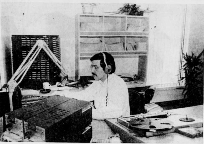 Black and white photograph of Michel Montminy hosting a radio program. He is wearing headphones and sitting in front of a microphone, surrounded by radio equipment.