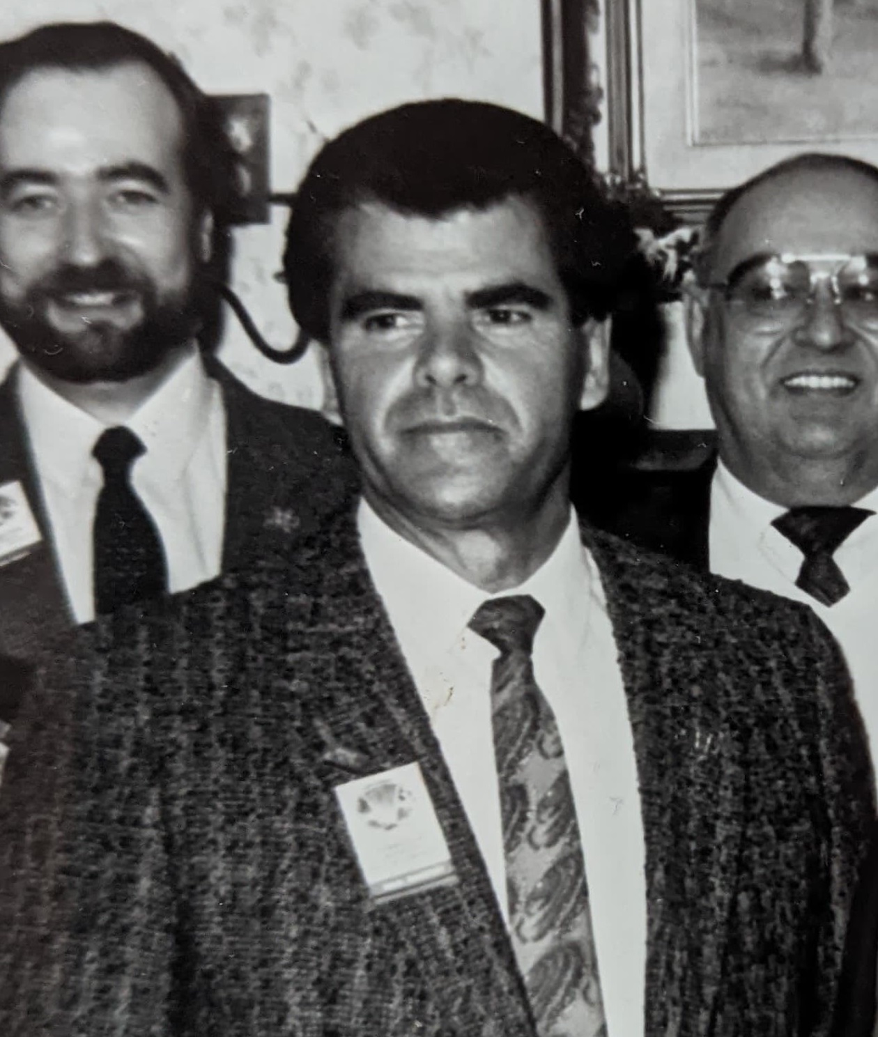 Black and white photograph of Marcel Messervier. He is wearing a striped jacket and a patterned tie. Two people in suits and ties are standing behind him.