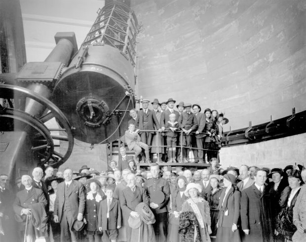 Black and white photograph of a large group of people in front of a very large telescope.