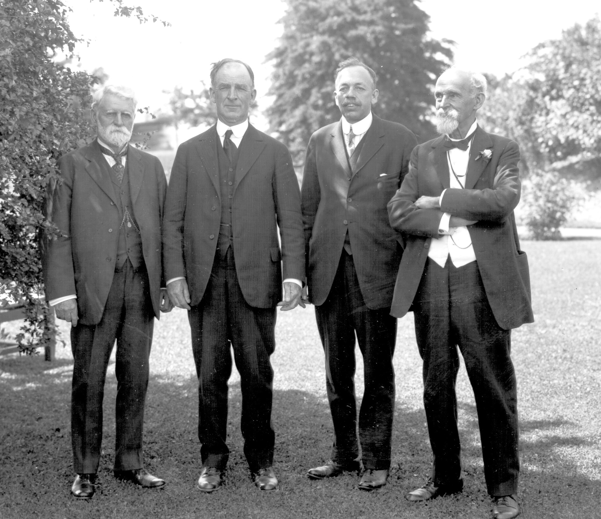 A black and white photograph of four well-dress gentlemen circa 1920 standing on a lawn