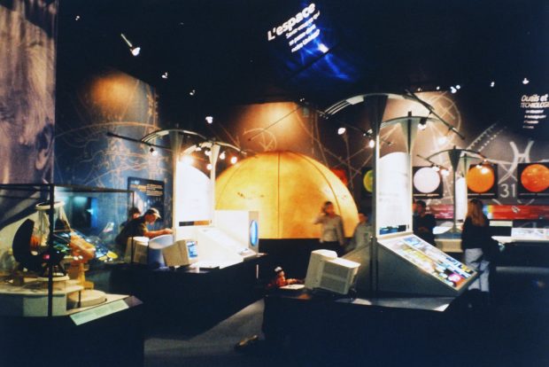 The interior of an astronomy visitor centre. A model of a large telescope, informative displays and a planetarium dome that looks like the Sun are visible.