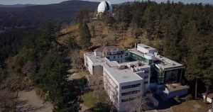 A drone photograph of a very large building on a hill side. On top of the hill is a white telescope dome.