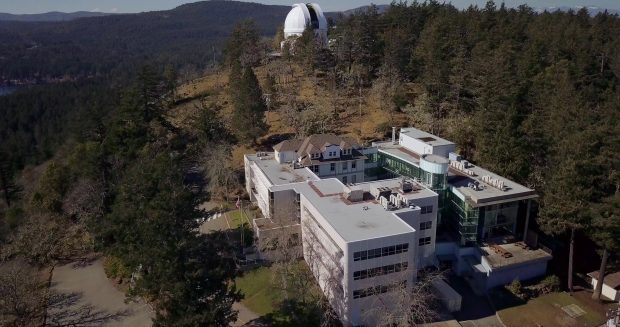 A drone photograph of a very large building on a hill side. On top of the hill is a white telescope dome.