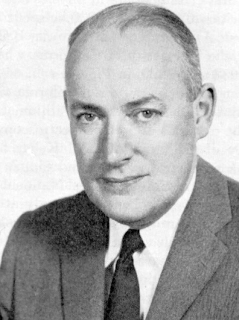 Black and white portrait photograph of a man wearing a jacket and tie