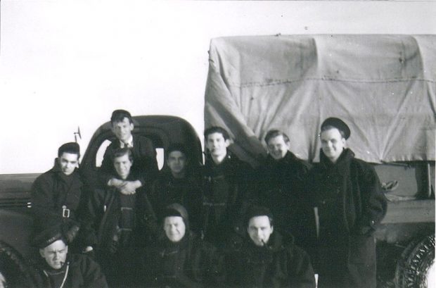 A black and white photograph of ten Navy Officers posing in front of a covered Navy truck.