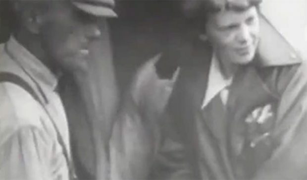 Amelia Earhart standing by plane with unknown man before takeoff.