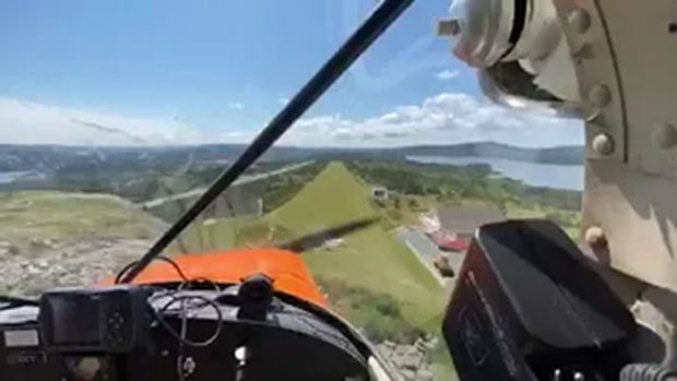 A coloured photo from inside a flying small aircraft as it approaches a grassy airstrip to land.