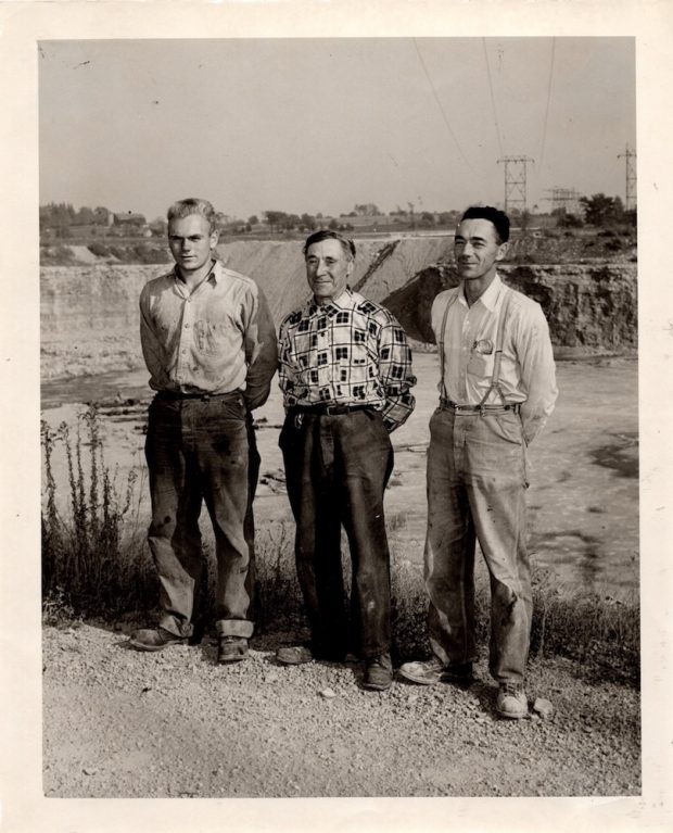 Black and white photograph of three men standing together at the edge of a quarry pit