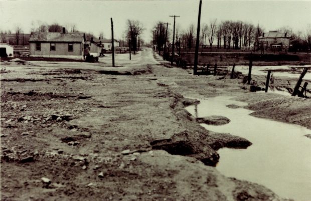 A view up a flooded street with puddles in the foreground and a few buildings on the left