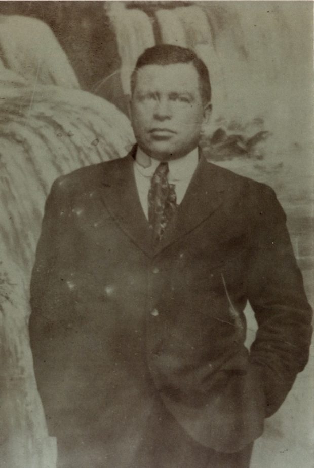 A black and white portrait of a man in a suit and tie with his hands in his pockets