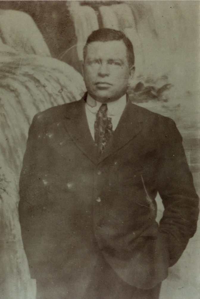 A black and white portrait of a man in a suit and tie with his hands in his pockets