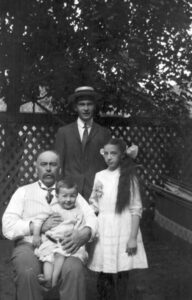 Black and white photograph of Dr. Hanly sitting outside with his children Arthur, standing behind him, Lois, standing beside him, and Bruce, sitting on his lap.