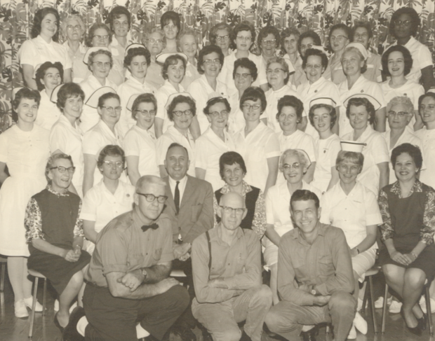 Black and white photograph of nurses posing for a photograph at the Almonte General Hospital. Three rows of nurses are standing and one row of nurses is seated. There are three men in the front row.