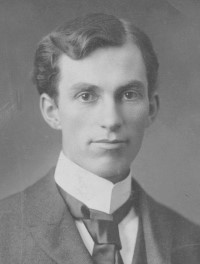 Black and white photographic portrait of John Francis Dunn, a young man with dark hair wearing a white shirt, jacket and tie.