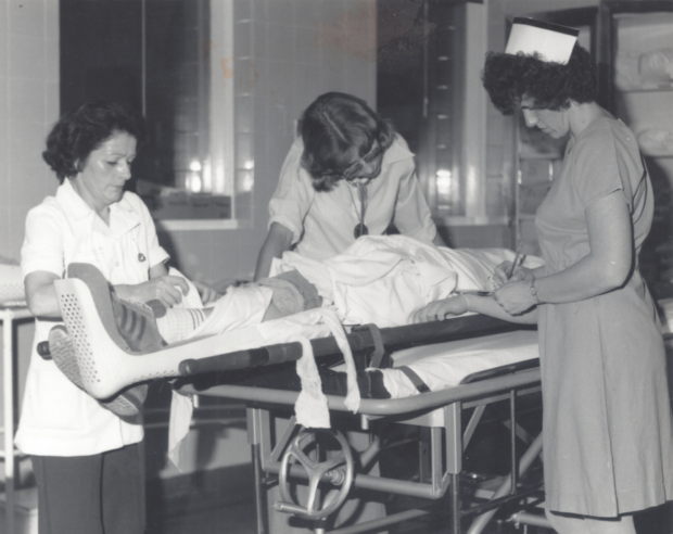 Black and white photograph of two nurses and a doctor caring for a patient on a stretcher.