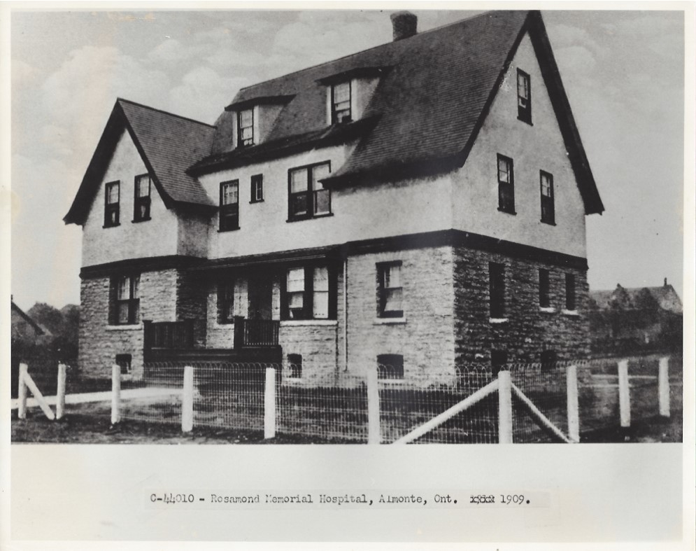 Black and white photograph of a three-story building. A fence surrounds the building and there is a pathway leading to the front steps.