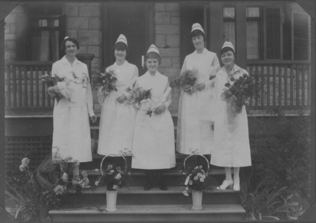 Black and white photograph of five women wearing nursing uniforms and holding bouquets of flowers.