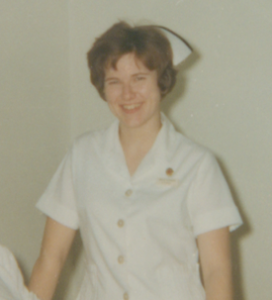 Colour photograph of a woman wearing a nursing uniform and smiling at the camera.