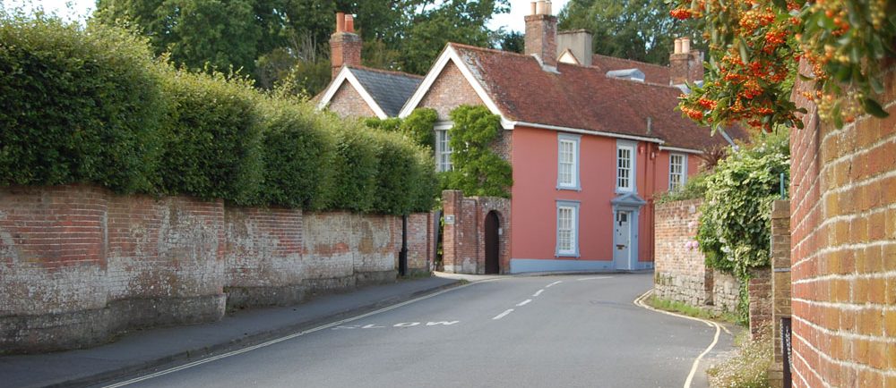 Colour photograph of a pink house on a curved road with a brick fence