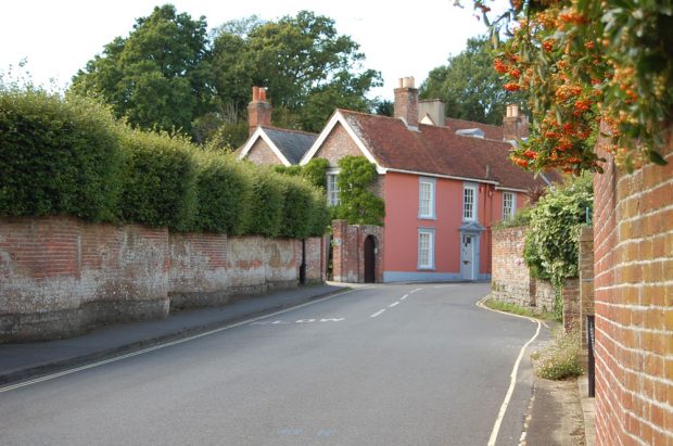 Colour photograph of a pink house on a curved road with a brick fence