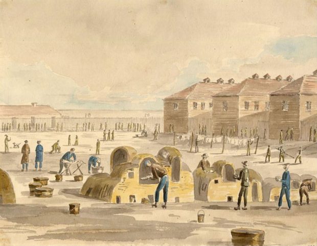 Three barracks buildings are at the back of the open square within the walls. On the square several prisoners are baking bread in outdoor ovens.