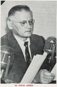 A 1930's black and white photograph of a man with glasses and holding a script, in a pegboard recording booth, speaking into a large microphone.