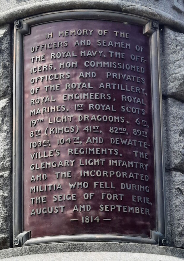 Plaque on a round stone memorial cairn. The plaque is maroon metal with gray print.