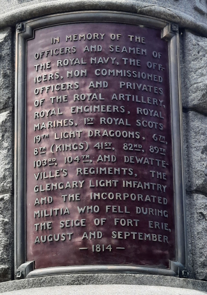 Plaque on a round stone memorial cairn. The plaque is maroon metal with gray print.