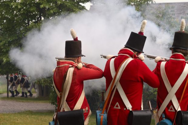 Three soldiers in red jackets shooting at a group of American soldiers