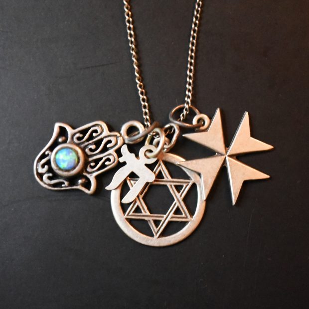 Gold pendants on a thinly chained necklace carry the Star of David, Iron Cross, Jewish character, and Harma hand bearing an iridescent blue stone.