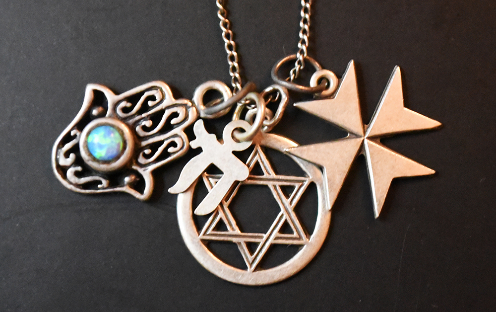 Gold pendants on a thinly chained necklace carry the Star of David, Iron Cross, Jewish character, and Harma hand bearing an iridescent blue stone.