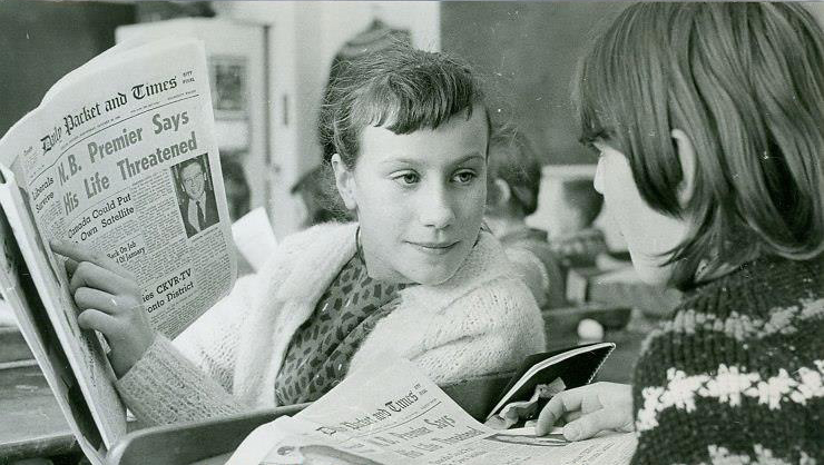 Vintage black and white photograph circa 1960 of two young school girls reading The Packet and Times together in class. One girl points to an article as the other takes notice.