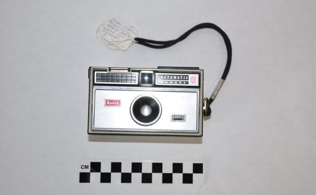 Small, rectangular, silver Kodak Instamatic Camera 100 with red details and black wrist strap, circa 1963.