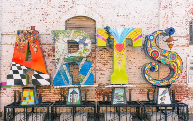 Large, colourful letter sculptures from Streets Alive artists help spell, Arts District in front of a sun-bleached brick wall downtown Orillia.