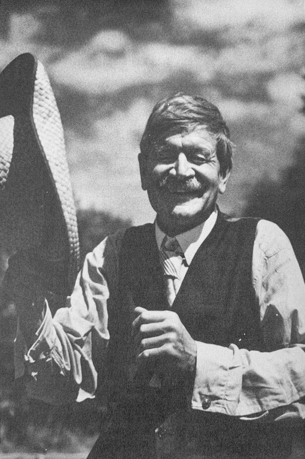 Black and white photograph of Stephen Leacock outdoors, laughing with his farm hat in hand, circa 1941