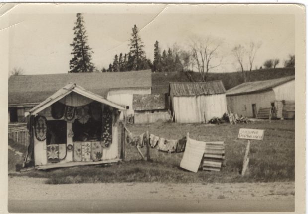 Black and white photo of a carpet stall in front of farm buildings.