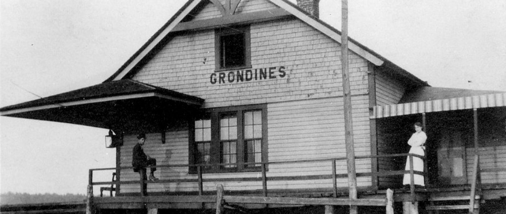 Black and white photo of a woman standing and a man sitting on the gallery of the Grondines train station.