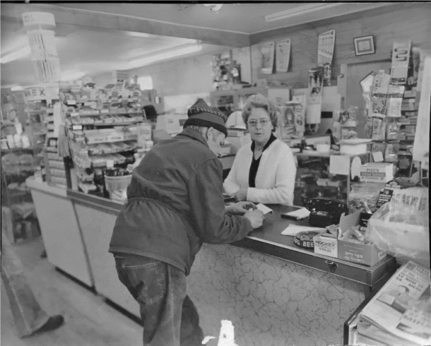 Black and white photo of a woman and a man at the checkout counter of a general store.