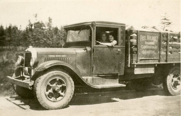 Black and white photo of two women driving a vintage truck.