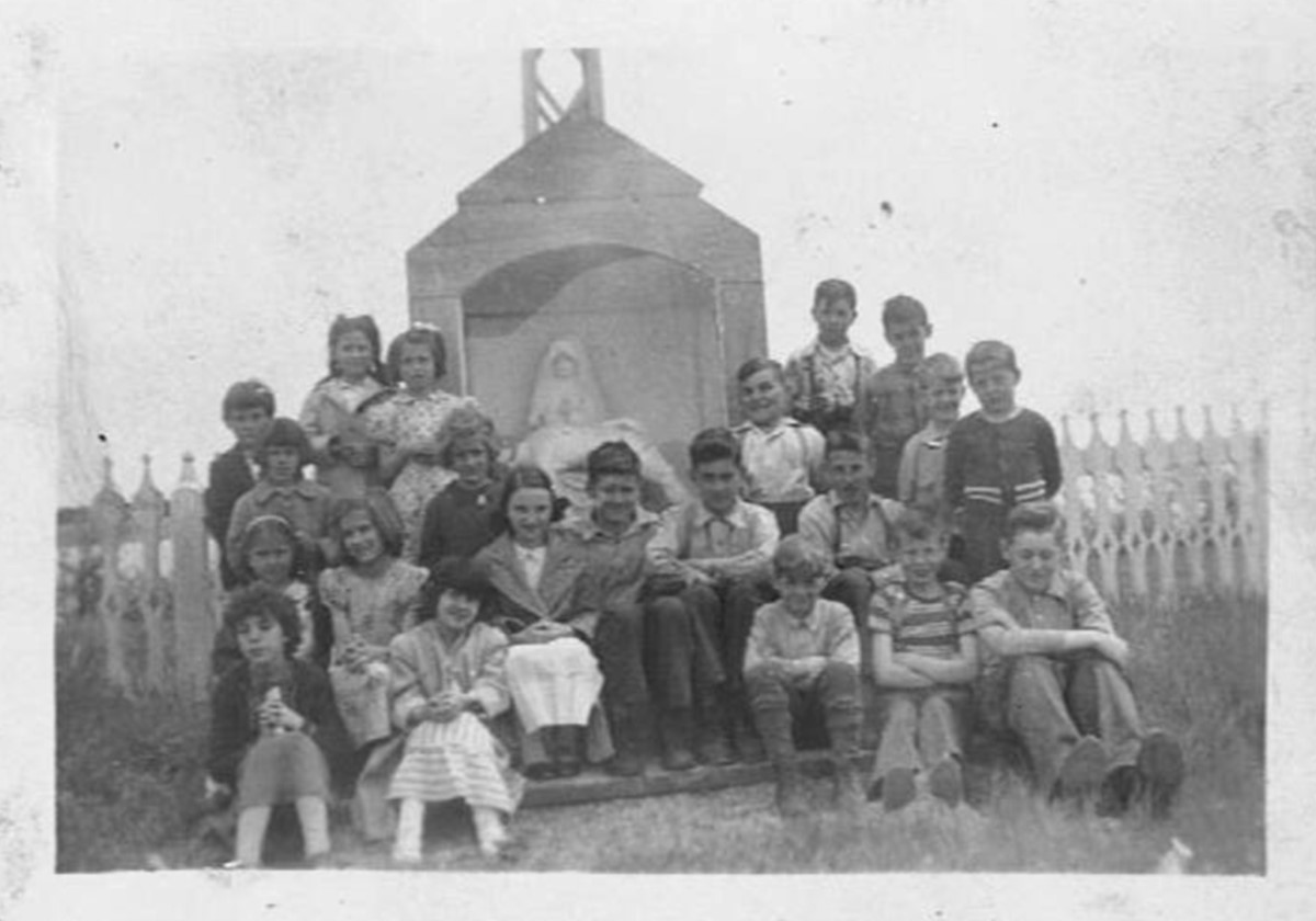 Black and white photo of a group of children sitting outside.