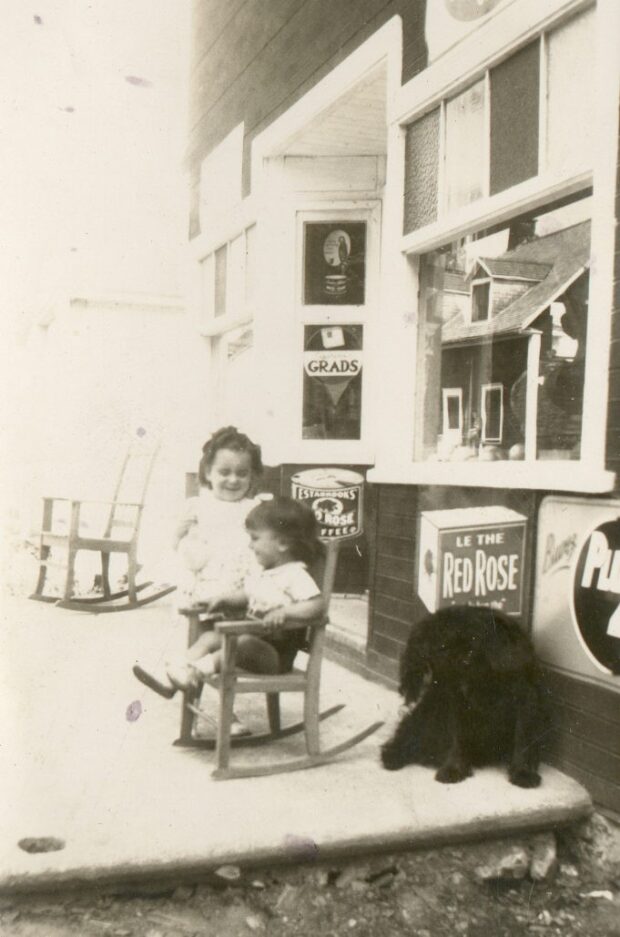 Black and white photo of two children and a dog in front of a grocery store.