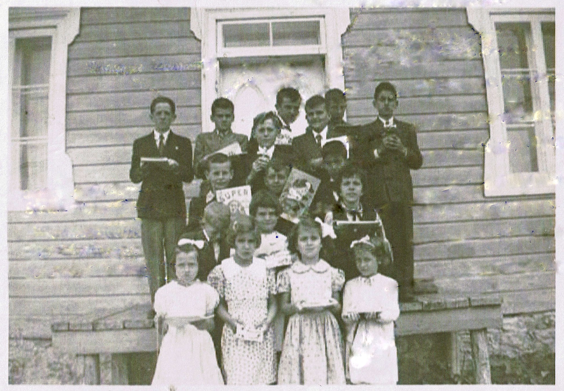 Black and white photo of a group of children holding a book in front of the school.