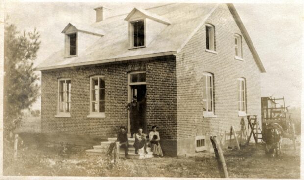 Black and white photo of four people in front of a brick house.