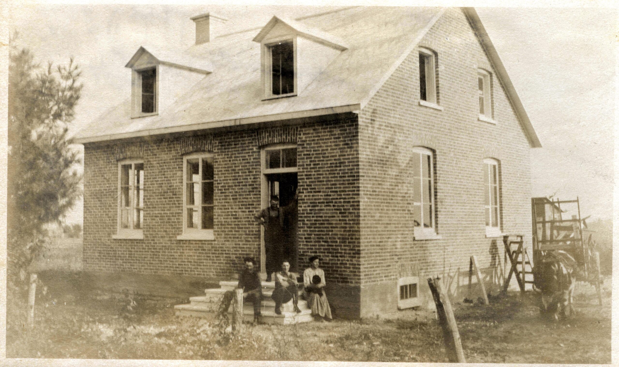 Black and white photo of four people in front of a brick house.