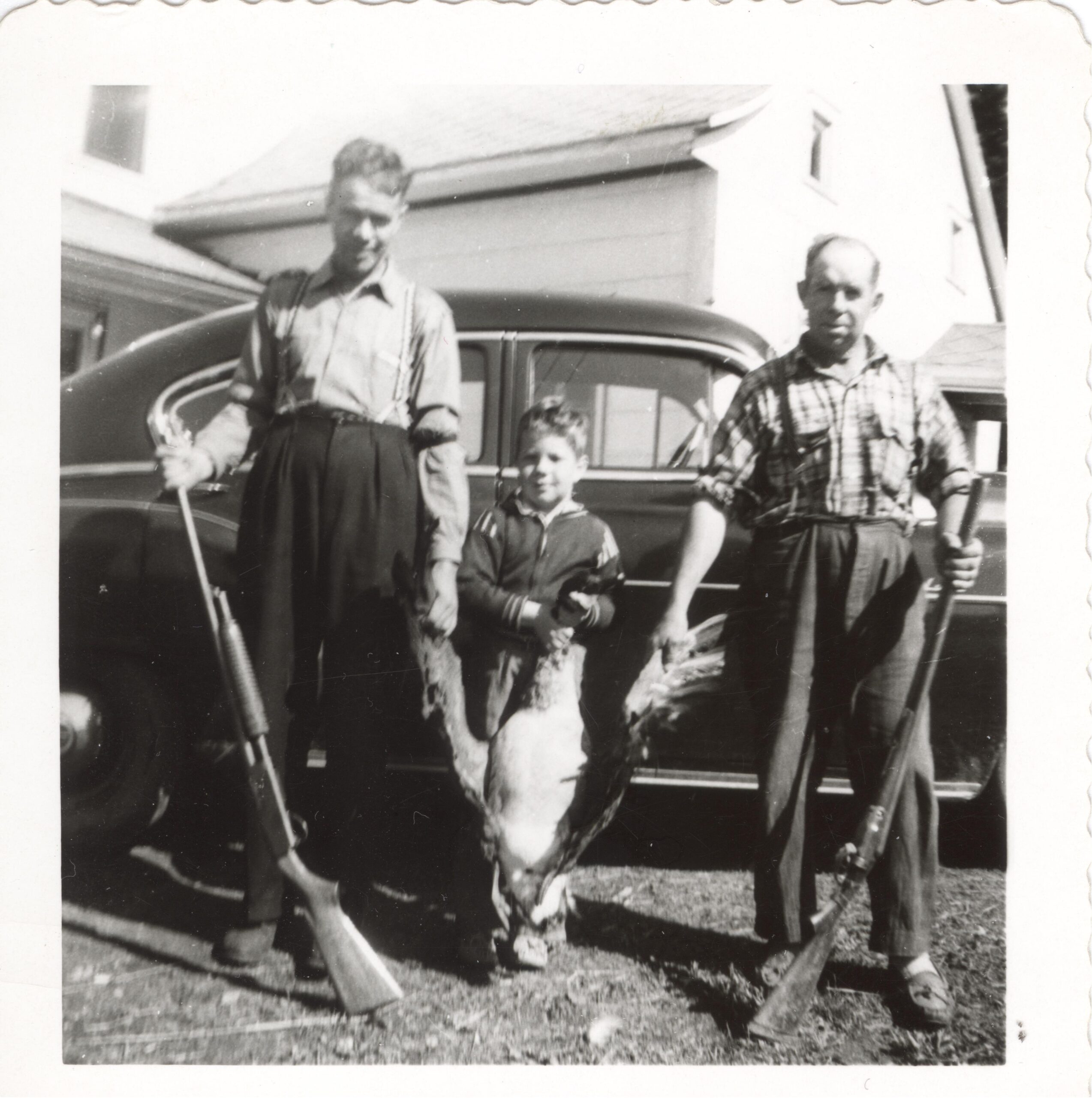 Black and white photo of two men and a child holding a bustard.