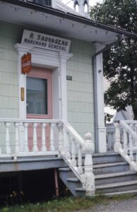 Photo of the pink door of a general store. Above the door is inscribed “R. Sauvageau - marchand général”.