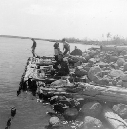 Black and white photo of five men fishing at the end of the wharf.