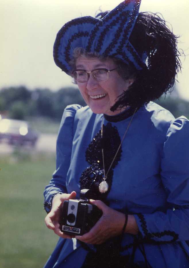 Thérèse Sauvageau in a historic blue dress holding a camera.