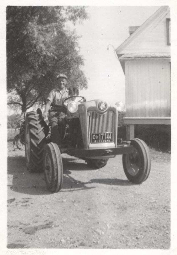 Black and white photo of a man sitting on a tractor.