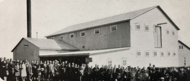 Black and white photo of a group of people in front of a two-storey factory.